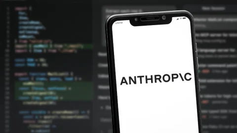 Ekranında ANTHROPIC yazısı bulunan bir telefon, arka planda kod görüntüleri