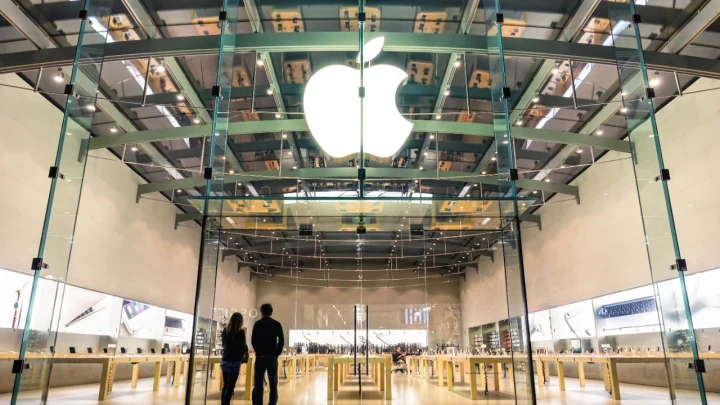 Cam cepheli bir Apple mağazasının girişinde ışıklı Apple logosu