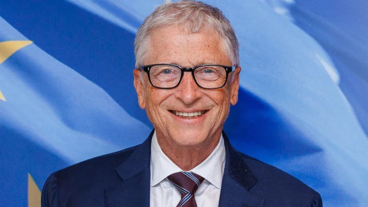 Bill Gates, mavi arka plan önünde takım elbisesiyle gülümsüyor