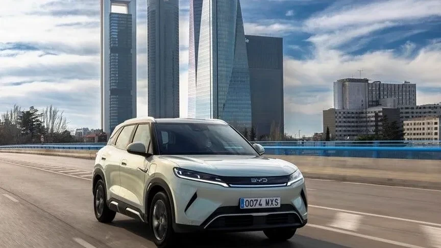 Şehir silüeti önünde yolda ilerleyen beyaz BYD elektrikli SUV