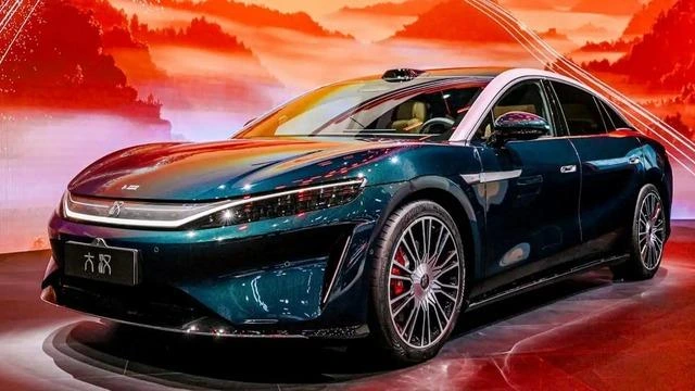 Kırmızı tonlarda bir arka plan önünde sergilenen koyu yeşil BYD Great Han sedan