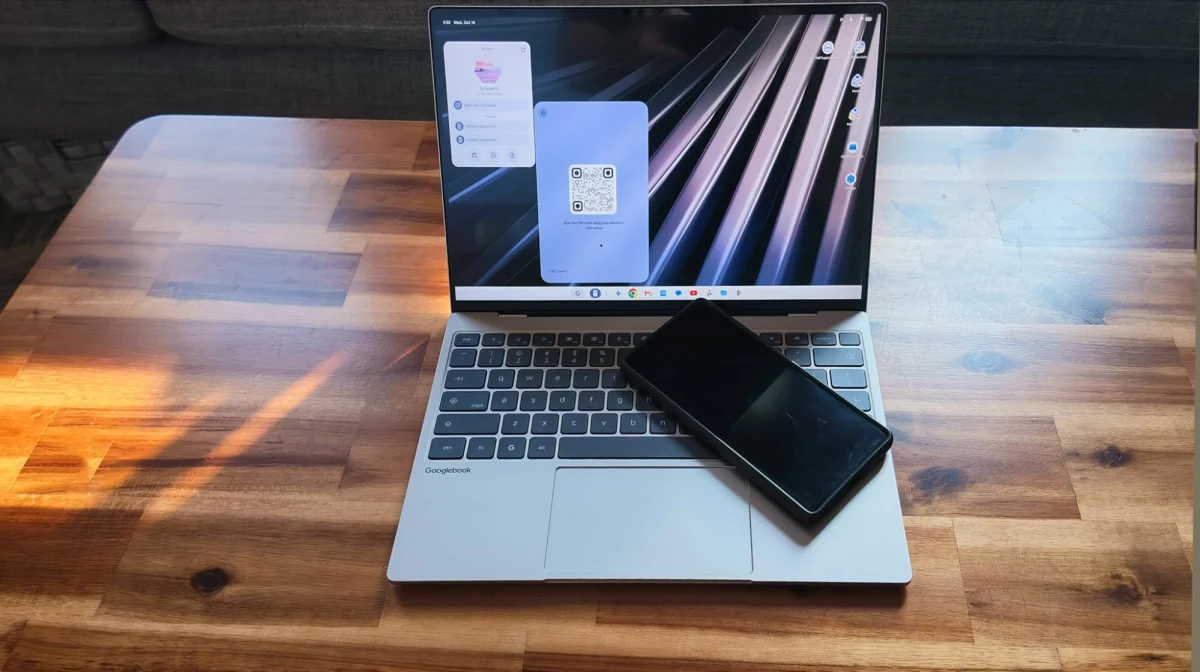 Ahşap masa üzerinde açık dizüstü bilgisayar ve önünde duran akıllı telefon