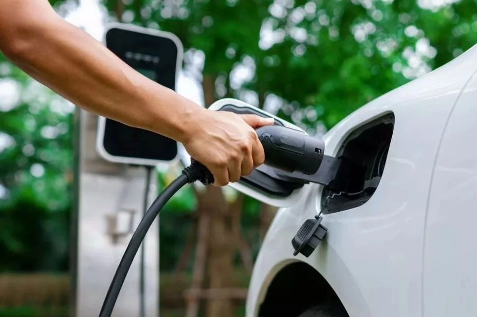 Bir kişi elektrikli otomobilin şarj kablosunu araca takıyor