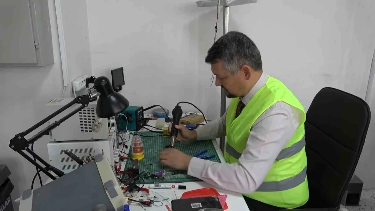 Parlak yelek giyen bir kişi elektronik ekipmanların bulunduğu masada çalışıyor