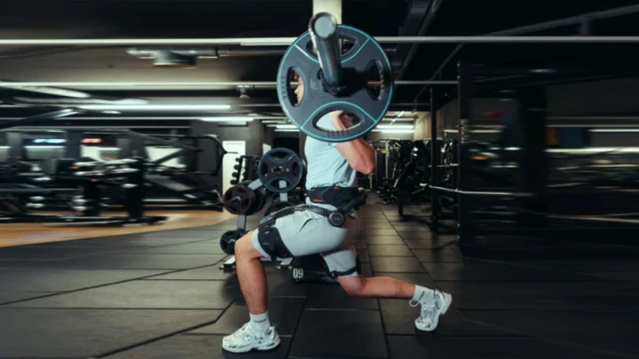 Spor salonunda ağırlık çalışması yapan bir kişinin bel ve bacak bölgesinde giyilebilir dış iskelet sistemi görülüyor.