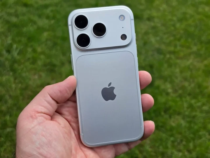 Bir kişinin elinde tuttuğu, arka yüzü ve kamera modülü görünen açık renkli iPhone