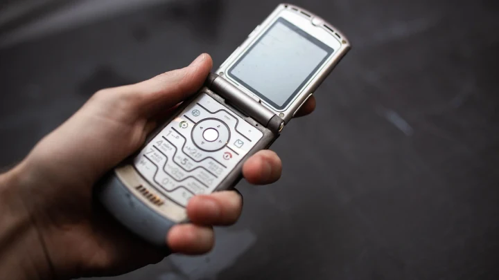 Bir kişinin elinde açık halde tuttuğu eski tip kapaklı cep telefonu