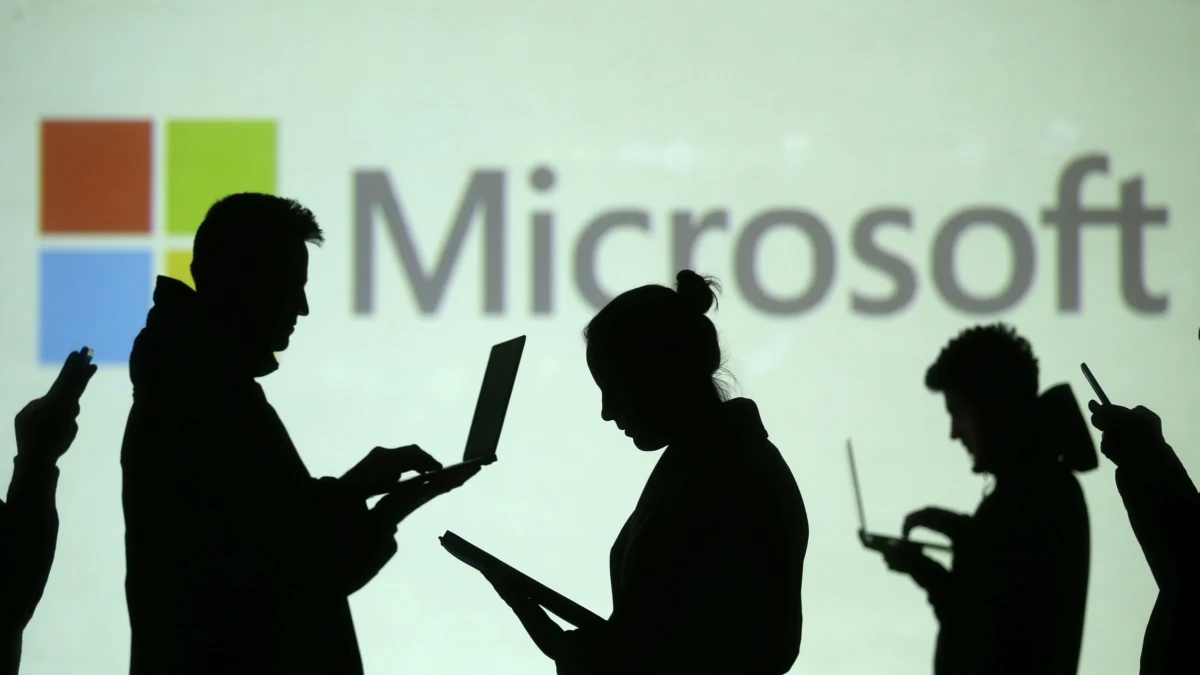 Microsoft logosunun önünde cihaz kullanan çalışanların siluetleri