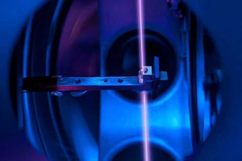 Nükleer saat deney düzeneğinde dikey mor lazer ışını ve mavi renkli optik bileşenler