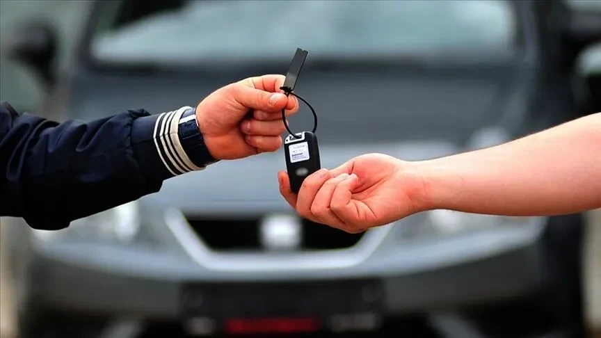 Bir otomobilin önünde iki el arasında uzatılan araç anahtarı