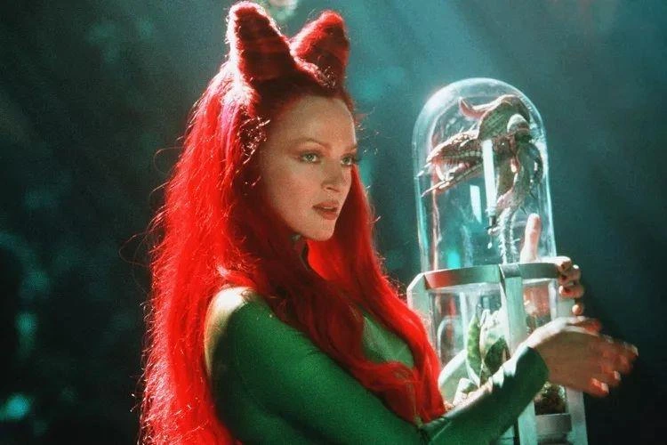 Kırmızı saçlı, yeşil kıyafetli Poison Ivy karakteri cam bir fanusu tutuyor.