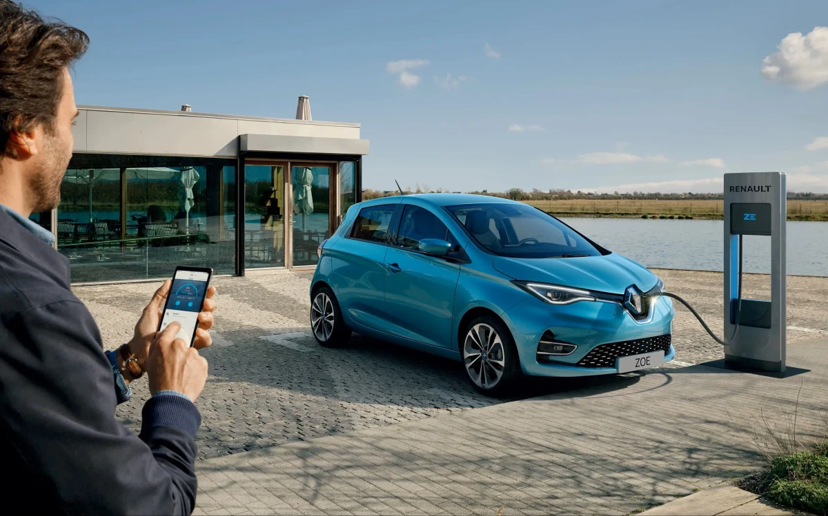 Bir kişi, şarj istasyonunun yanında duran mavi Renault elektrikli otomobilin fotoğrafını çekiyor