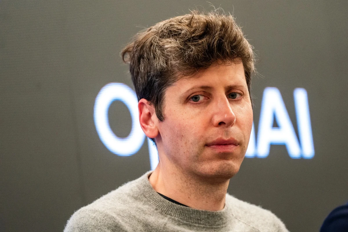Sam Altman, arka planda OpenAI yazısı bulunan bir ekranın önünde