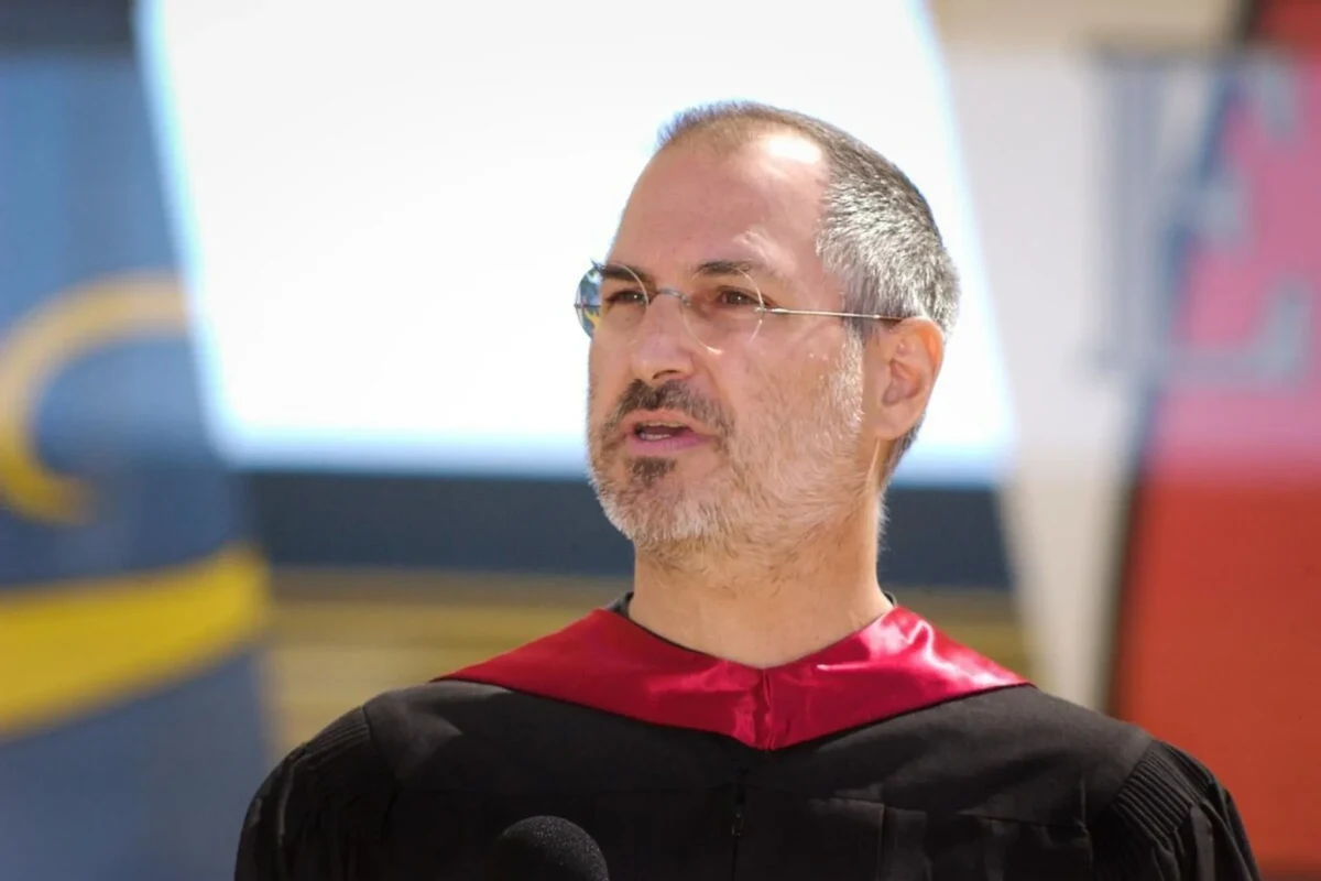 Steve Jobs, siyah cübbe ve kırmızı yakayla bir etkinlikte konuşurken