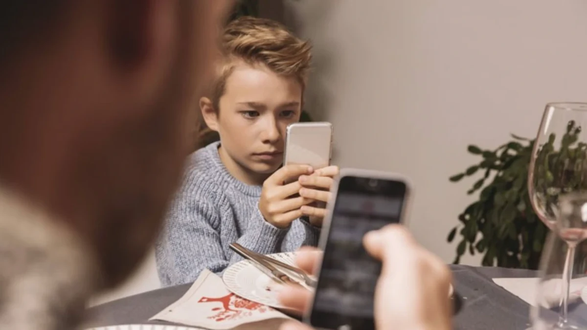Masada otururken telefon kullanan çocuk ve ön planda başka bir telefon
