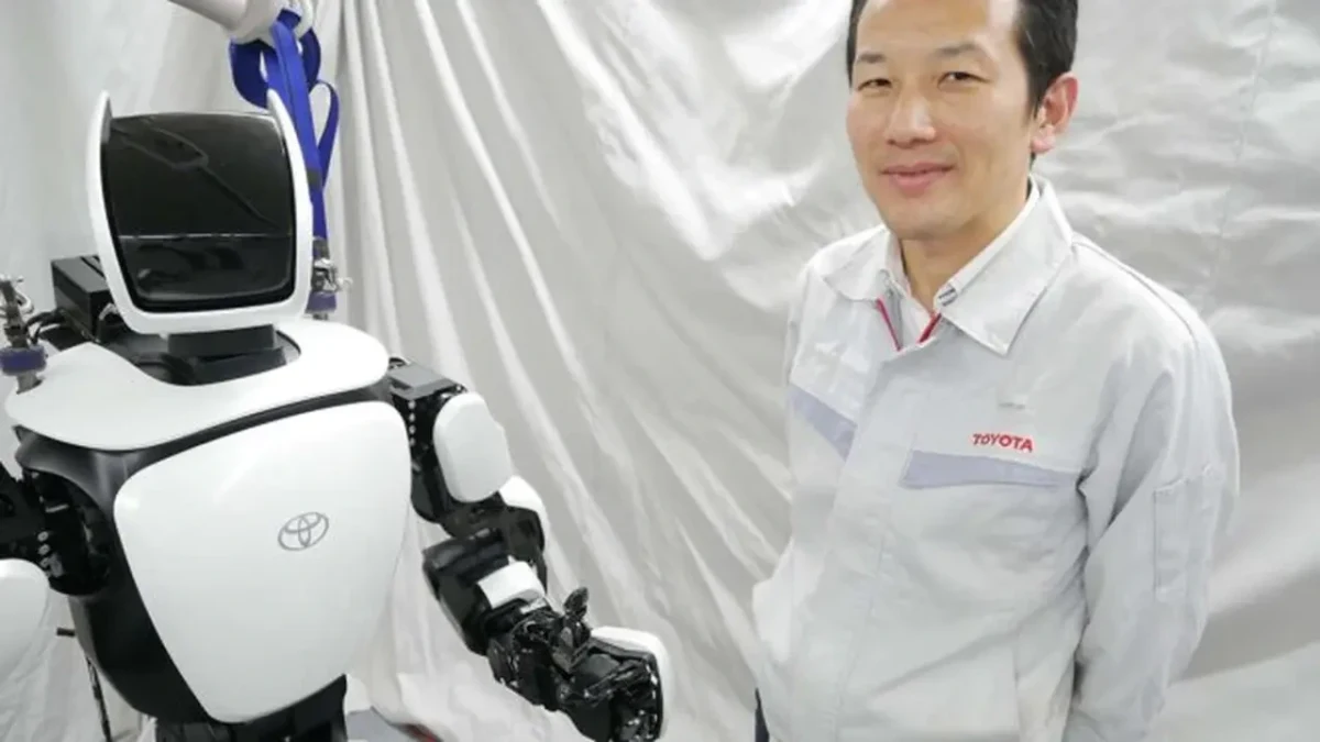 Toyota logolu beyaz bir robotun yanında duran Toyota çalışanı