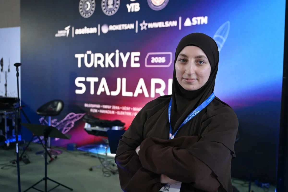 Siyah başörtülü genç kadın Türkiye Stajları 2025 yazılı tanıtım panosunun önünde duruyor