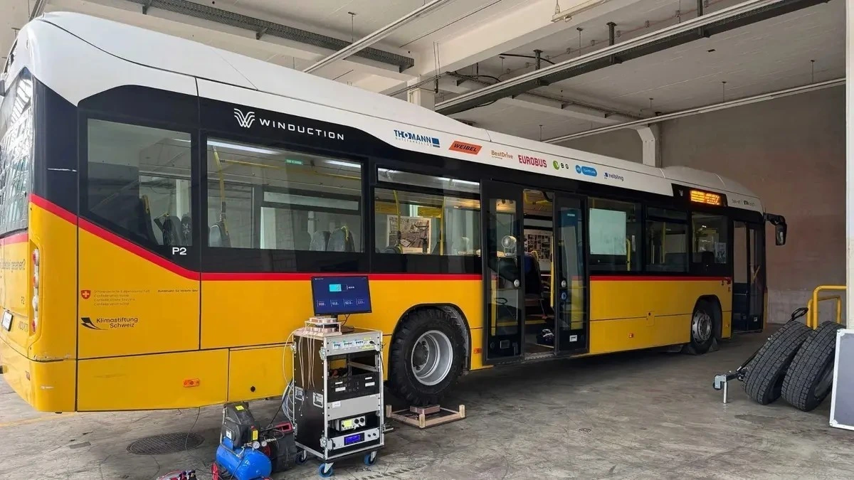 Winduction logosu bulunan sarı otobüs, kapalı bir alanda test ekipmanlarının yanında duruyor