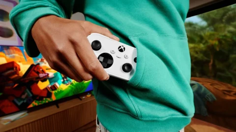 Turkuaz üst giyen bir kişinin elinde beyaz Xbox Nano kumanda